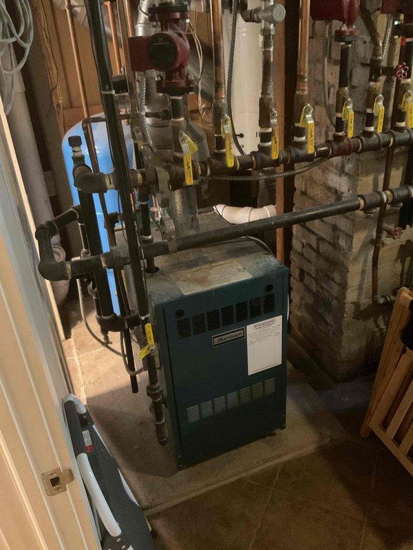 Responded to no hot water complaint and investigated 12-5 water heater displaying Error Code 3. Upon arrival, found Amtrol DX-69 pressure tank system with aged equipment that had been in service for over six years. Inspected the blue pressure expansion tank, associated copper piping connections, and digital control unit. During diagnostic evaluation, identified boiler system with critically low pressure affecting overall hot water production. Assessed the mechanical room containing teal-colored boiler unit with extensive black iron piping network, circulation pump, and multiple zone valves. Documented equipment conditions through photographs showing pressure tank installation, boiler configuration, and interconnected plumbing systems including copper and PVC components. Referred boiler pressure issue to HVAC department for proper system pressurization and further evaluation of heating system functionality, as the low boiler pressure was determined to be the root cause affecting hot wat