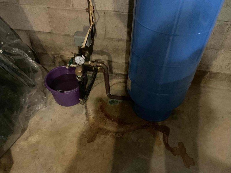Responded to customer request for water quality assessment. Collected water sample from existing treatment system for laboratory analysis. System consists of water softener unit and blue storage/treatment tank with associated copper piping, pressure gauge, and valve assembly. Observed signs of moisture accumulation on concrete floor near tank base with collection bucket in place beneath plumbing connections, indicating potential minor leak or condensation issue that may require follow-up once lab results are received to determine if additional treatment or system adjustments are needed.