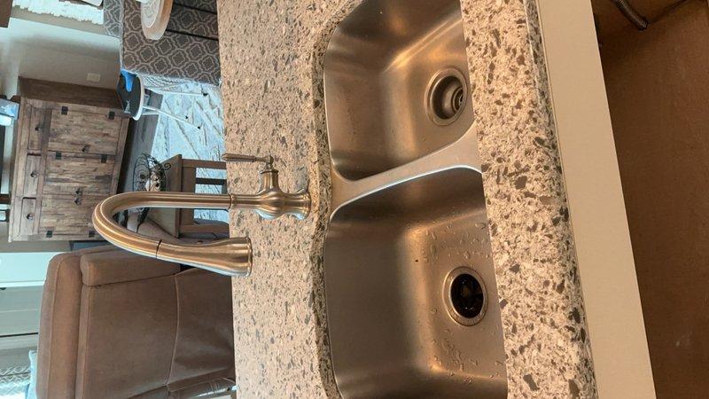Installed customer-supplied double-basin stainless steel kitchen sink with brushed nickel single-handle pull-down faucet in granite countertop. Additionally installed hot water recirculation pump system with PVC supply and return lines, pressure switch, isolation valves, and electrical connections in under-sink cabinet area to provide instant hot water delivery and reduce water waste.