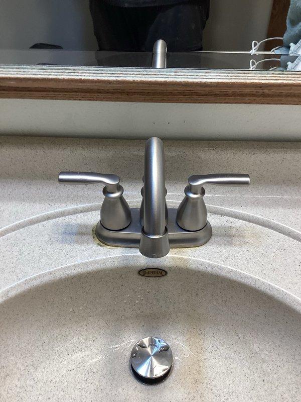 Installed customer-supplied brushed nickel lavatory faucet with center-set design and dual lever handles on bathroom sink. Completed installation included mounting faucet assembly to sink deck, connecting hot and cold water supply lines, and installing chrome pop-up drain assembly with proper sealing and alignment.