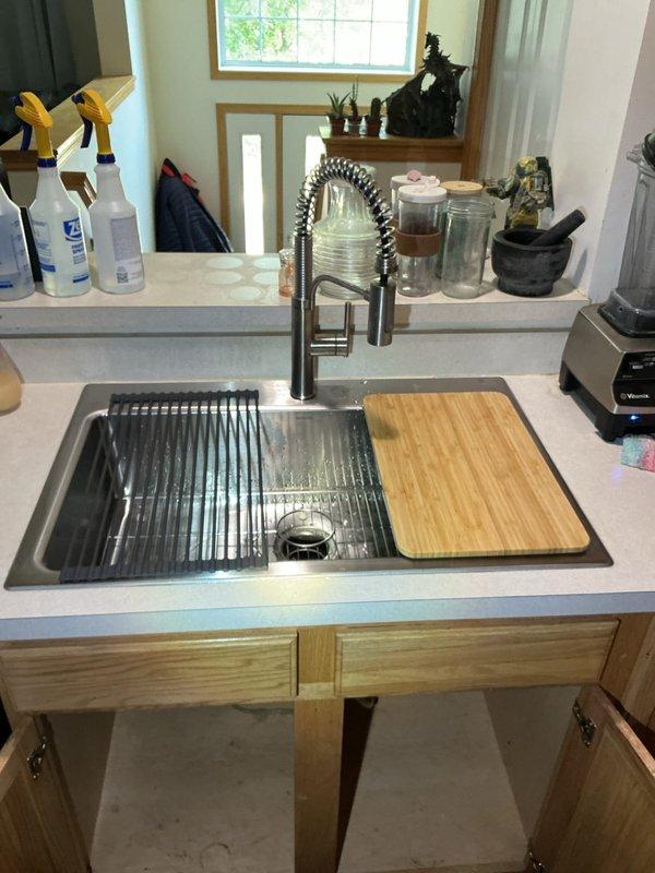 Completed kitchen sink replacement, transitioning from a double basin to a customer-supplied Kohler single basin undermount sink with integrated drying rack. Disconnected and removed existing faucet with side sprayer, garbage disposal, and PVC drain lines before extracting the old double basin sink. Installed customer-supplied single handle kitchen faucet with pull-down sprayer featuring coiled spring neck design and connected to existing water supply lines. Reconnected garbage disposal unit to new sink configuration and modified PVC drain assembly, including P-trap, to accommodate the change from double to single basin layout. Verified all plumbing connections for proper operation and leak-free performance, sealed perimeter of sink to countertop, and confirmed garbage disposal and faucet functionality. One-year workmanship warranty provided on installation.