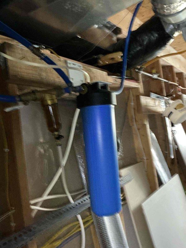 Completed comprehensive plumbing inspection of older farmhouse with extensive DIY installations. Documented existing water filtration system in crawl space, including blue cylindrical filter housing with brass fittings, sediment filter with clear bowl, and PEX piping distribution throughout structure. All accessible plumbing components, connections, and routing were visually examined and photographed for maintenance records.