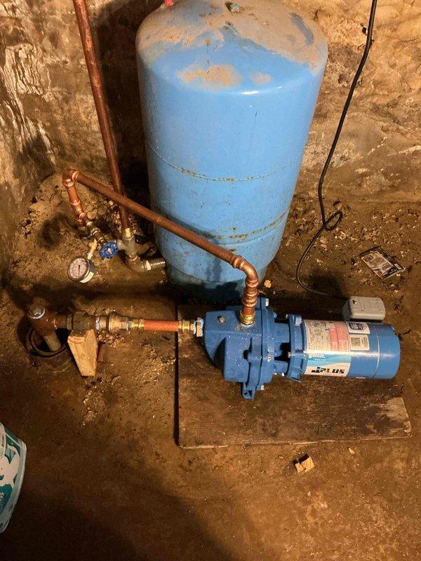 Sold and prepared for installation of whole house water filtration system including 1" inline spin-down sediment filter and 20" standard sediment/rust filter for residential well water application. Upon site assessment, discovered shallow well pump pit had dried out below the inlet point where the well pipe enters the ground, preventing immediate installation of the filtration equipment. System components were delivered and staged on-site. Property owner has arranged for new well installation by well drilling contractor. Filtration system installation will be scheduled and completed following well replacement work. Documented existing water pressure system configuration including aged pressure tank with visible surface corrosion and functioning electric pump assembly with copper piping and brass fittings.