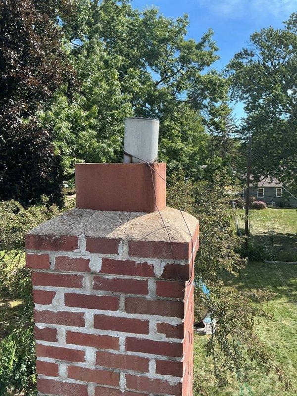 Completed installation of high wind resistant chimney rain cap on existing brick chimney structure. Contacted homeowner prior to arrival to confirm appointment scheduling. Accessed rooftop and removed existing standard metal flue cap from concrete chimney crown. Installed new white metal high wind rated chimney cap designed to prevent water intrusion and withstand severe weather conditions. Secured cap properly to concrete crown ensuring weather-tight seal. Verified proper fitment and stability of new rain cap installation. Inspected brick chimney structure and mortar joints during installation - noted masonry in functional condition with minor weathering and efflorescence present. Documented completed installation with photographs showing before and after conditions of chimney cap replacement. Installation completed within scheduled two-hour timeframe.