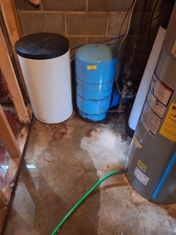 Responded to service call for leaking pressure tank in basement utility area. Upon inspection, confirmed active leak from aging blue pressure tank showing significant deterioration, surface corrosion, and wear. Water staining and rust-colored marks visible on concrete floor beneath equipment, indicating ongoing moisture exposure. Pressure tank exhibited compromised integrity requiring full replacement. Documented existing conditions including tank specifications, current pressure readings from mounted gauge, and plumbing connections to water softener and water heater systems. Photographed deteriorated tank exterior, tank tee assembly, and associated piping infrastructure. Submitted part order form to obtain estimate for new pressure tank and tank tee assembly replacement. Customer advised that water supply did not require emergency shutoff at time of inspection.