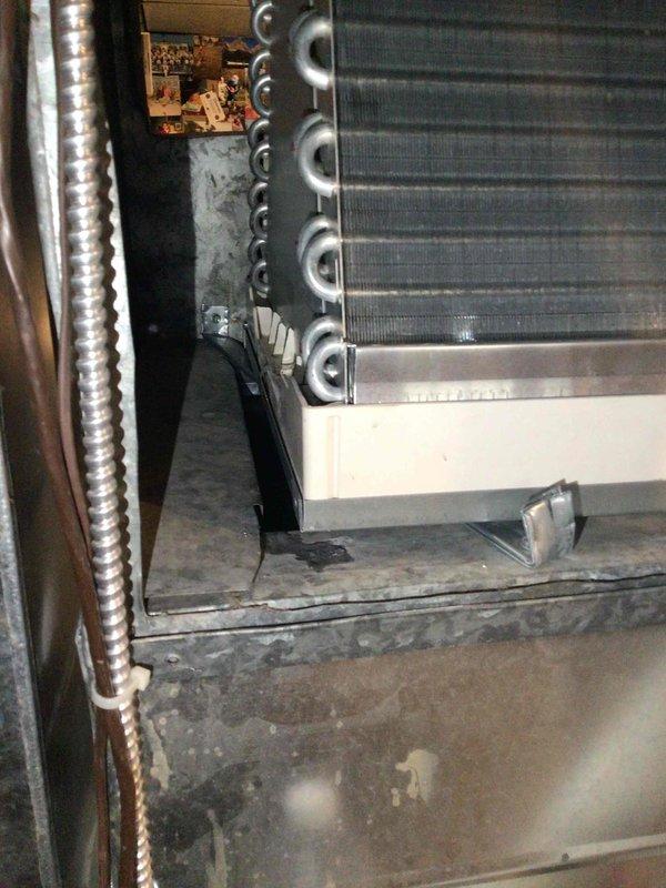 Responded to no-cool call on 1-year-old ICP system with reported water leakage pooling in furnace and overflowing onto floor. Upon inspection, discovered evaporator coil had tilted backward, preventing proper condensate drainage from the drain pan. Installed shim screw underneath coil assembly to adjust pitch forward, restoring proper drainage angle. Verified condensate now flows correctly through drain line without pooling or overflow. System operating normally with no further leakage observed.