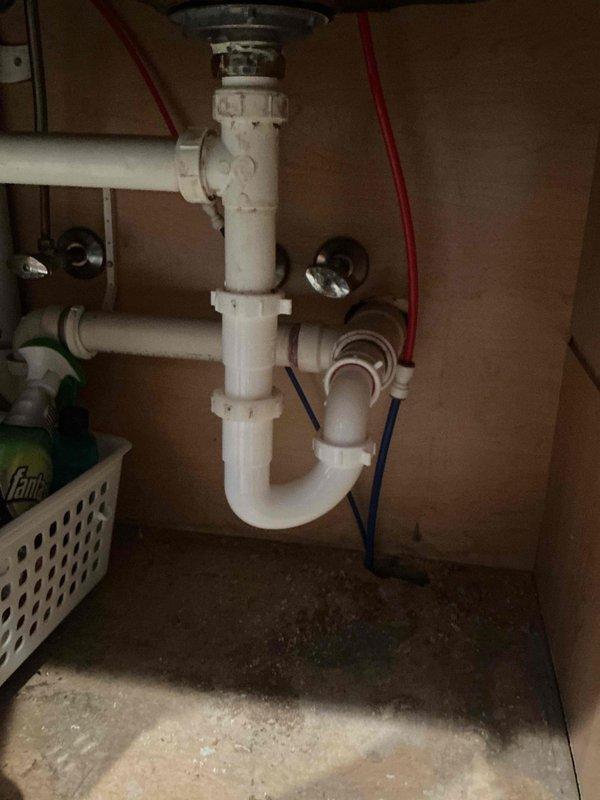Responded to service call for leaking reverse osmosis system with water pouring from blue drain hose connection point. Replaced defective P-trap assembly and reconnected RO drain line to eliminate leak. Installed new drain components to restore proper function and prevent future water damage beneath sink.