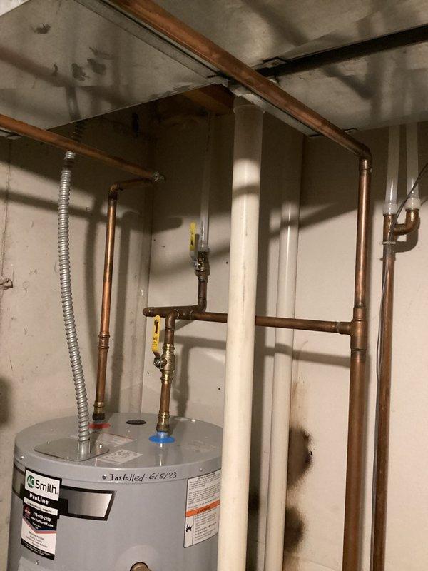 Completed comprehensive plumbing inspection of residential property as part of recurring maintenance program. Documented water heater installation dated June 5, 2023, including copper supply lines, gas connections with yellow-handled shut-off valves, and flexible gas line routing. Identified multiple service needs including bathroom sink drain operating sluggishly due to partial obstruction in P-trap assembly, utility sink faucet requiring valve adjustment or replacement due to stiff operation, and toilet seat needing replacement with ivory standard model. Noted audible squeaking noise originating from plumbing system when shower is activated, likely caused by water hammer or loose pipe mounting. Photographed water heater installation showing proper gas line configuration and under-sink plumbing assembly with PVC drain connections for documentation and future reference.