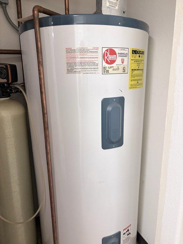 Responded to service call for loud popping and explosive noises coming from electric water heater. Upon inspection, identified a large 119.9-gallon Rheem electric water heater experiencing severe sediment buildup causing thermal expansion noises during heating cycles. Performed complete tank flush to remove accumulated mineral deposits and sediment from bottom of tank. Documented equipment condition with photographs showing existing water heater and adjacent water softener system. Recommended replacement of both water heater and water softener unit due to age and condition of equipment, with follow-up estimate scheduled for full system replacement.