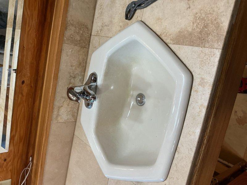 Responded to a call for a continuously dripping bathroom faucet in a corner-mounted pentagonal lavatory sink. Upon inspection, determined the existing 20-year-old two-handle chrome faucet had failed internal components causing the persistent leak. Removed the old faucet assembly and installed a new chrome two-handle lavatory faucet with matching drain assembly. Verified all supply line connections were secure, tested both hot and cold water lines for proper flow and shut-off function, and confirmed no leaks were present at the faucet base or supply connections. The new installation was completed successfully with no further dripping or leakage issues.