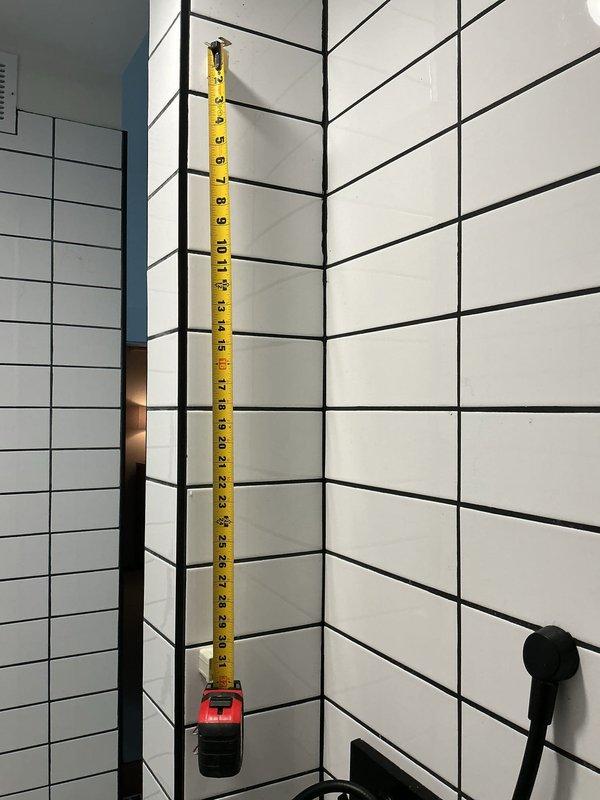 Completed plumbing inspection identifying loose toilet requiring repair. Installed new 4-inch PVC flange on concrete floor to secure toilet fixture. Took measurements for future shower bar installation in tiled shower area with subway tile pattern.