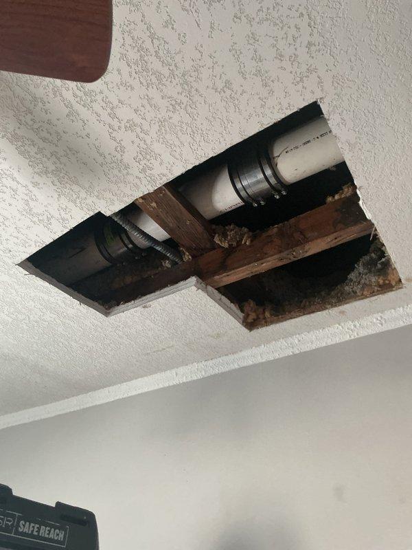 Responded to warranty callback for persistent leak at roof leader and secondary roof leak. Upon inspection through ceiling access panel, discovered failed repair at 6" roof drain leader caused by structural deficiencies including lack of support under 90-degree elbow and severe backpitch condition. Water accumulation in leader created stress fracture at previous repair point. Installed two mission bands to accommodate stress and movement at leak points. Applied pressure testing to roof drain to verify repair integrity. Documented conditions showing water damage to wooden joists and ceiling materials. Repair completed successfully under warranty conditions. Presented options for permanent replacement versus temporary repair solution due to underlying structural and drainage pitch issues.