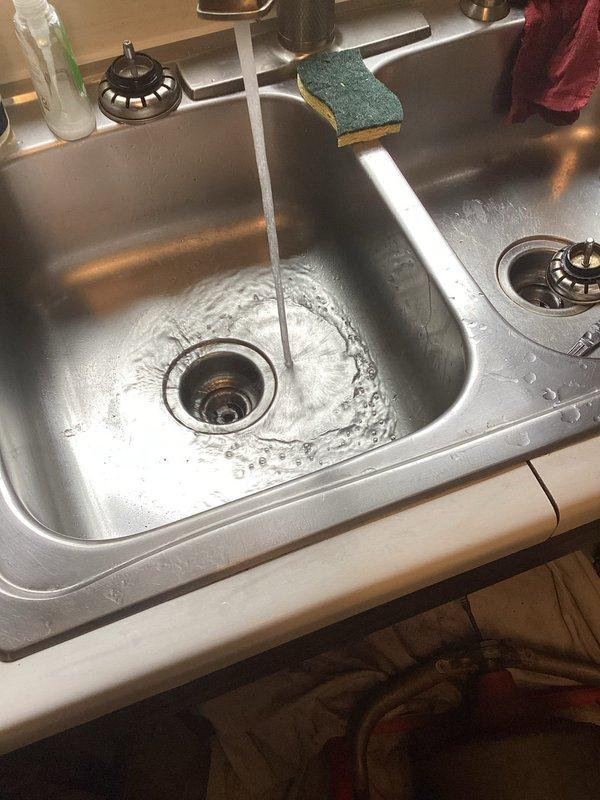 Responded to a recurring kitchen sink drain blockage that had been previously serviced less than a month prior. Accessed the drain system through the cabinet base and utilized mechanical cable equipment to clear the obstruction in the drain line. Upon completion, tested water flow through both basins of the double-bowl stainless steel sink to verify proper drainage and confirm the blockage was fully removed.