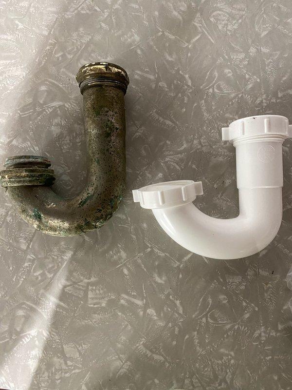 Responded to emergency water leak at laundry sink caused by corroded chrome P-trap that had rusted through completely. The existing metal P-trap assembly exhibited extensive corrosion with green patina and mineral buildup, rendering it unable to maintain a proper seal. Upon inspection, discovered the old fitting had failed due to age-related deterioration and could not be realigned to stop the leak. Removed the compromised metal P-trap assembly and installed new white PVC P-trap with slip-joint connections, restoring proper drainage function and eliminating the water leak. Tested the new installation to confirm leak-free operation, allowing full restoration of water usage for laundry and other household needs.