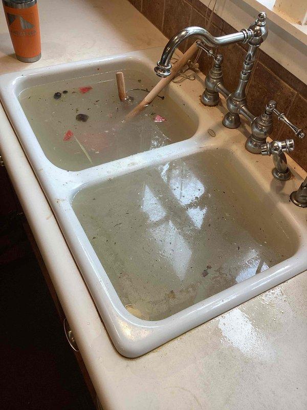 Responded to a clogged kitchen sink with both basins completely blocked and holding standing water. Upon arrival, found that the homeowner had attempted to clear the stoppage using plungers and by operating the garbage disposal without success. Inspection revealed rice debris as the primary cause of the blockage in the drain line. Deployed drain cable equipment to snake and clear the kitchen drain line, successfully removing the obstruction and restoring proper drainage to both sink basins. Verified full water flow and drainage function upon completion.