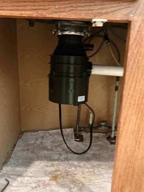 Responded to an active water leak originating from a failing garbage disposal unit beneath the kitchen sink. Upon arrival, confirmed the existing disposal was the source of the leak, which had been temporarily contained by the customer. Removed the old defective garbage disposal unit from the sink mounting assembly. Installed a new garbage disposal unit with electrical cord, ensuring proper alignment with the sink drain flange and secure mounting. Connected the discharge pipe to the existing drain line configuration. Completed all electrical connections and verified proper operation of the new unit. Performed a comprehensive leak test by filling the sink and running water through the disposal while checking all connection points and seals. Confirmed no leaks were present at the mounting flange, discharge connection, or any plumbing joints. Verified full functionality of the disposal unit. Left the workspace clean with all connections secure and the system operating properly.