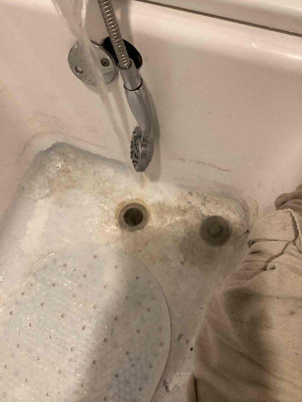 Responded to clogged bathtub drain call and found standing water with visible soap buildup and mineral scale accumulation around dual drain openings. Successfully cleared blockage using cable snake equipment to remove hair, soap residue, and scale deposits obstructing the drain line. Verified proper drainage flow and confirmed full restoration of normal bathtub function upon completion.