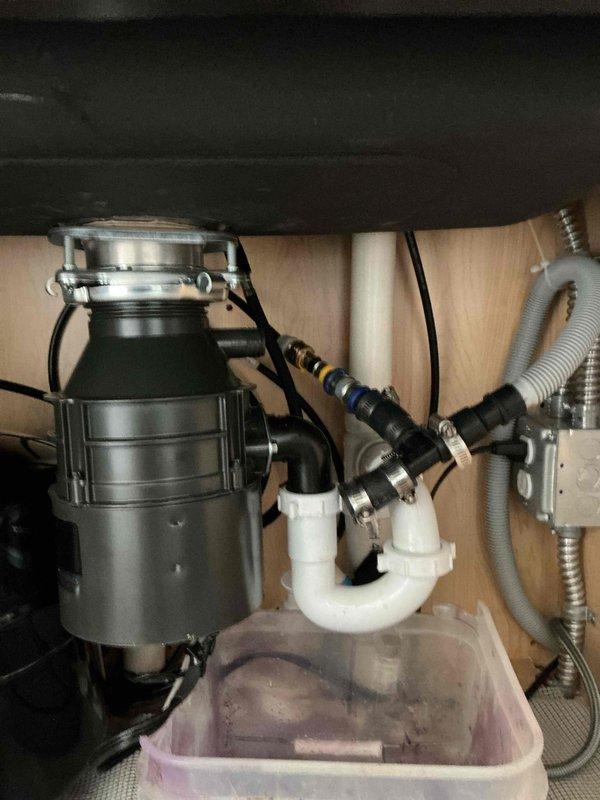Responded to service call for garbage disposal leak and dishwasher drainage issue following recent disposal installation. Upon diagnostic inspection, identified that the dishwasher drain knockout plug had not been removed from the disposal inlet, preventing proper drainage and causing the dishwasher to overflow. Additionally, discovered the disposal unit was insufficiently tightened at the mounting assembly, resulting in water leakage through the basket strainer connection. Removed the knockout plug from the disposal's dishwasher inlet port and verified unobstructed drainage flow. Properly secured and tightened the disposal mounting assembly to eliminate leakage at the sink flange connection. Tested both the dishwasher drain cycle and disposal operation to confirm all issues were resolved and system was functioning correctly with no further leaks detected.