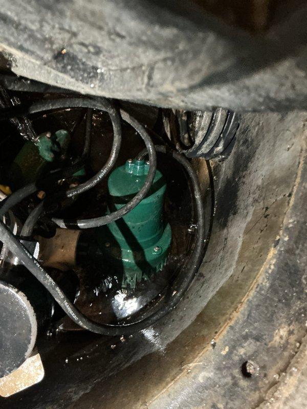 Performed comprehensive inspection of residential sump pump system per customer request. Examined submersible pump unit installed in concrete pit, verified proper operation and positioning, and assessed water level conditions. Inspected complete discharge piping system including vertical PVC discharge line with quiet check valve, confirmed secure mounting and proper connections at basin interface. Evaluated battery backup system components including wall-mounted control unit, battery charger, and backup pump assembly to ensure emergency operation capability. All electrical connections, power cords, and control systems were visually inspected for proper installation and functionality. System found to be operational with all components functioning as designed.