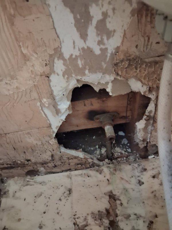 # Plumbing Service - Broken Toilet Stub Out

Responded to service call for leaking pipe in bathroom. Upon arrival, performed thorough inspection of the affected area and identified a broken toilet stub out as the source of the water leak. The toilet flange connection had fractured, with the stub out pipe broken off at the structural framing level.

Documented extensive water damage to surrounding wall surfaces, including deteriorated drywall, delaminated paint layers, and compromised plaster materials in the corner section where walls meet. Inspection revealed the damaged PVC plumbing line running through the wall cavity behind compromised surface materials. Access opening exposed wooden structural framing and the full extent of the broken pipe connection.

Provided comprehensive assessment of repair requirements, including removal of damaged wall materials, replacement of broken toilet stub out fitting, proper reconnection to existing plumbing line, and restoration of wall surfaces. R