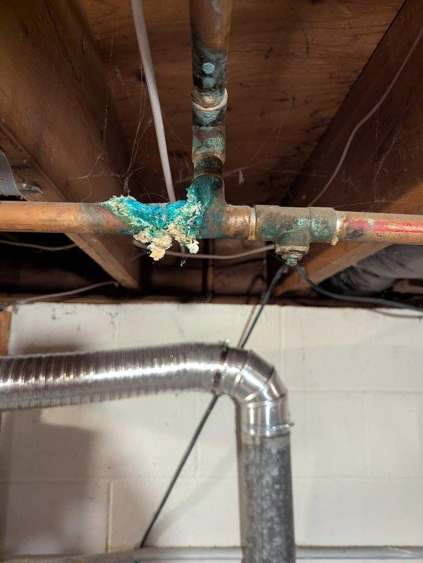 Responded to service call for visible slow leaks in hot water heating system piping prior to heating season. Upon inspection, identified severely corroded copper pipe joints with extensive verdigris buildup and mineral deposits at T-junction fittings in basement utility area. Documented multiple compromised joints showing advanced copper oxidation and active leak points through comprehensive photography. Determined repairs required specialized heating system expertise and coordinated with HVAC department for proper boiler system servicing and joint repair to prevent system failure during upcoming heating season.