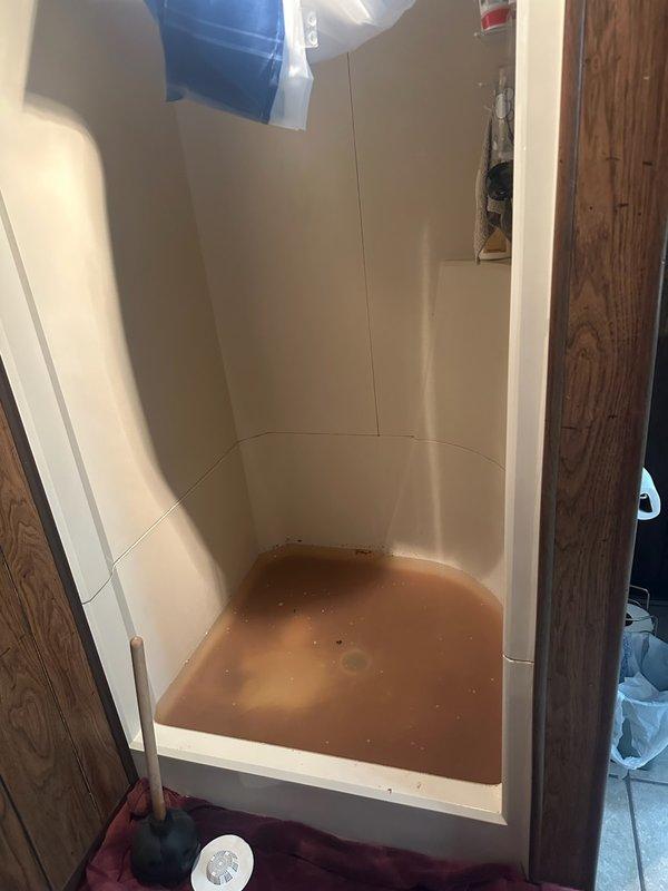 Responded to a basement bathroom emergency involving backed-up shower and toilet fixtures. Upon arrival, found approximately 4 inches of standing water with rust-colored sediment in the shower base and a non-draining toilet. Initial customer attempts with chemical drain cleaner and plunger had been unsuccessful and caused cross-contamination between fixtures, indicating a main line blockage.

Deployed rigid drain cleaning machine to snake the main drainage line. Located and removed a cloth or diaper obstruction at 27 feet from the access point. Continued mechanical cleaning to address approximately 3 feet of solid grease buildup in the pipe downstream from the initial blockage. Successfully cleared the line and restored proper drainage to all affected fixtures. Documented site conditions with photographs showing the standing water discoloration and shower pan condition prior to service completion.