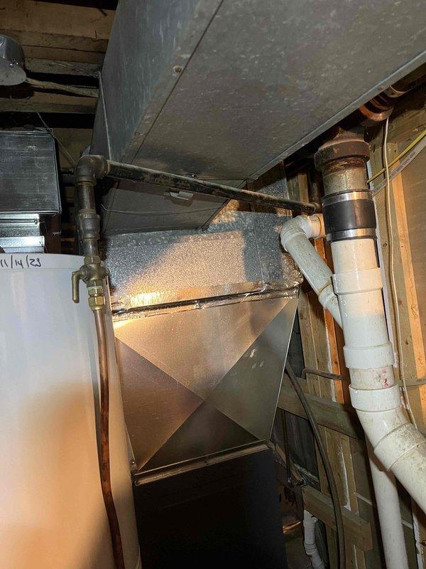 Responded to service call to investigate water condensation issue in furnace area. Upon inspection, located source of water as a rusted metal evaporator coil drain pan on 1987 HVAC system. Drain pan was improperly tilted backward, causing water accumulation. Temporarily propped up drain pan to correct angle and performed water test to assess leak severity. Testing confirmed significant leaking from corroded pan. Explained to homeowner that replacement drain pan for this vintage system would be extremely difficult to source due to age and discontinuation of parts. Documented conditions with photographs showing ductwork, drain pan assembly, and surrounding plumbing components. Recommended full AC unit replacement as most viable repair option given system age and parts availability constraints. Coordinated with sales advisor to schedule equipment replacement quote.