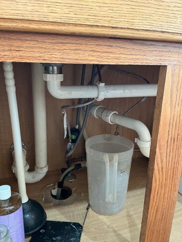 Responded to a backed-up kitchen sink that was causing water to overflow into the dishwasher. Upon inspection, found the kitchen sink drain line severely clogged with grease and debris buildup. Snaked the kitchen sink drain to clear the obstruction and restore proper drainage function. Photographed the under-sink plumbing configuration showing the garbage disposal, P-trap assembly, and drain connections for service documentation.