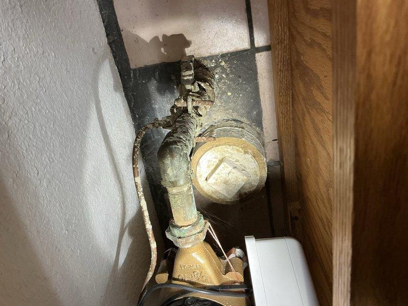 Responded to service call for reported water heater leak in utility space. Upon inspection, discovered standing water in confined crawl area beneath floor with aged plumbing infrastructure showing significant deterioration. Assessed tanked water heater and surrounding plumbing components, including copper piping with compromised insulation and corroded surfaces. Determined primary issue was main drain line blockage under floor or outside building rather than water heater failure. Black waste pipe showed severe insulation degradation with exposed sections, and brass fittings displayed age-related patina and discoloration. Photographed deteriorated conditions including damaged pipe insulation, confined utility space configuration, and affected plumbing components for documentation. Advised customer that standing water resulted from plugged main line causing drainage backup in floor drain rather than water heater malfunction. Scheduled follow-up appointment for professional drain cleaning