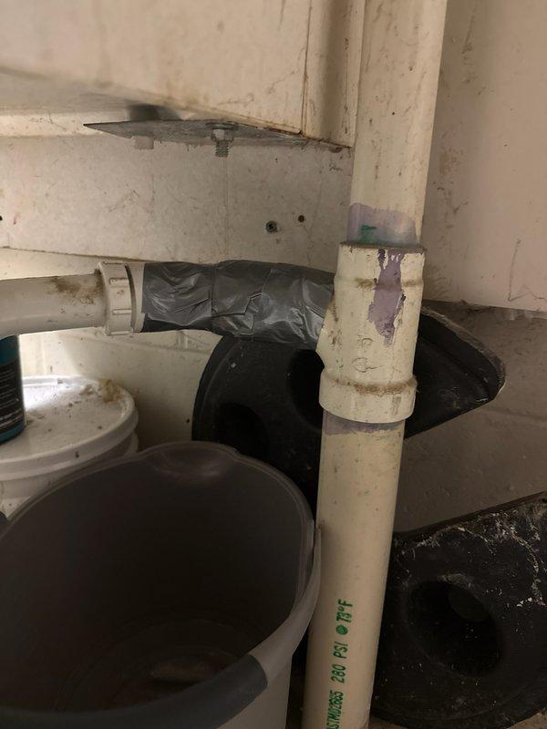 Responded to laundry tub drainage failure caused by cracked PVC drain tee fitting on the discharge line. Upon inspection, identified multiple deteriorated PVC fittings in the drain assembly connecting to the main sewer line prior to its entry into the concrete foundation. The drain tee on the right side of the laundry tub exhibited structural failure, and additional compromised sections were found in the taped areas of the drainage system. Temporarily secured the damaged sections to prevent sewer gas infiltration and allow completion of the washer cycle. Scheduled complete replacement of the laundry tub assembly including basin, faucet, supply stops, and drain piping to restore proper functionality and eliminate further drainage issues.