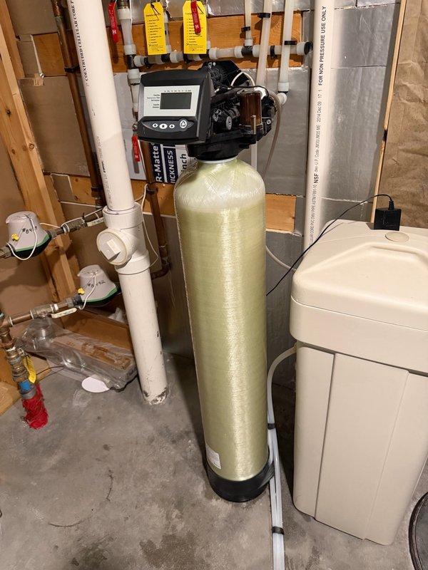 Responded to low water pressure complaint affecting the upper level of a 10-year-old residence. Upon arrival, confirmed that water pressure issues occurred only when the water softener was in service, with normal pressure restored when the system was bypassed. Performed diagnostic testing on the water softener system and identified that the softener control head was malfunctioning and not fully shifting during regeneration cycles, restricting water flow and causing reduced pressure throughout the upper level plumbing fixtures. The control head's failure to complete proper valve positioning prevented water from passing through the system at full volume. Provided estimate for replacement of the defective softener control head and complete resin bed replacement to restore proper system operation and water pressure. Documented equipment condition with photographs showing the existing water softener tank, brine tank, control head assembly, and associated plumbing connections. Submitted serv