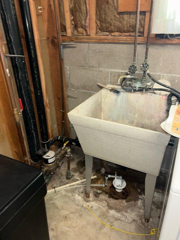 Responded to a basement leak complaint traced to the furnace humidifier system. Upon inspection, discovered the condensate drain line was completely plugged with rust buildup from previous coils, along with accumulated dirt and debris. Utilized vacuum equipment to clear the blockage, requiring multiple passes to fully restore proper drainage flow. Documented conditions with photographs showing the drain opening and surrounding utility area.