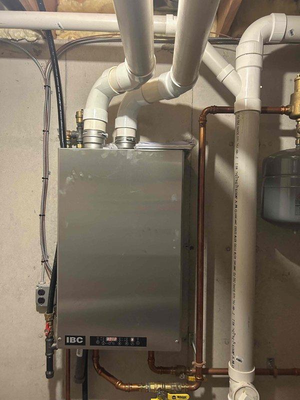 Responded to service call for in-floor heating system with suspected stuck valve and unusual hot water issues on a six-year-old IBC boiler. Upon investigation, system was producing excessive noise and releasing significant amounts of water when air bleeding was attempted. Diagnosed failed air valve (Schrader valve) on the expansion tank as the root cause of the problem. Replaced the defective Schrader valve with new component, bled air from the system, and conducted full operational testing to verify proper function. System restored to normal operation with no further issues detected.