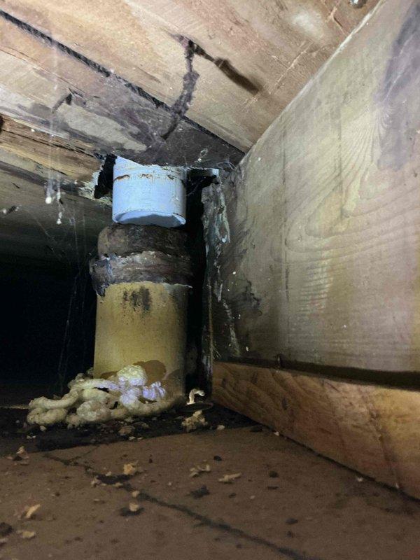 Responded to a drainage emergency in a 1941-era home where a deteriorated cast iron waste pipe had dropped approximately 5 inches from its original position, causing complete backup of all drains into the basement. Upon inspection, found the aged cast iron pipe had failed at a joint connection, with visible signs of corrosion and structural compromise. Documented the extent of damage through photographs showing the displaced pipe, surrounding water stains on wooden structural members, and temporary foam sealant material at the floor penetration point. The failed section exhibited significant discoloration and deterioration consistent with 80+ year-old cast iron plumbing. Assessed the existing plumbing configuration, which included a mix of original cast iron, PVC drain lines, and various connecting components mounted to wooden backing. Provided a comprehensive estimate for complete pipe repair and replacement of the compromised cast iron section to restore proper drainage function and 