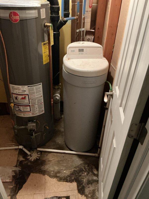 Responded to a water softener leak at a vacant property where the unit and main water line had been shut off as a precautionary measure. Conducted diagnostic inspection of the water treatment system and identified active leaking from the intake connection on the water softener head assembly. Upon further examination, discovered significant mold growth surrounding the softener head unit, indicating prolonged moisture exposure. Due to the extent of water damage and biological contamination present, recommended complete water softener replacement rather than repair. No repair work was performed on-site; documented findings with photographs showing the affected equipment, visible floor staining from water damage, and overall system condition. Case forwarded for water softener replacement quote and installation scheduling.