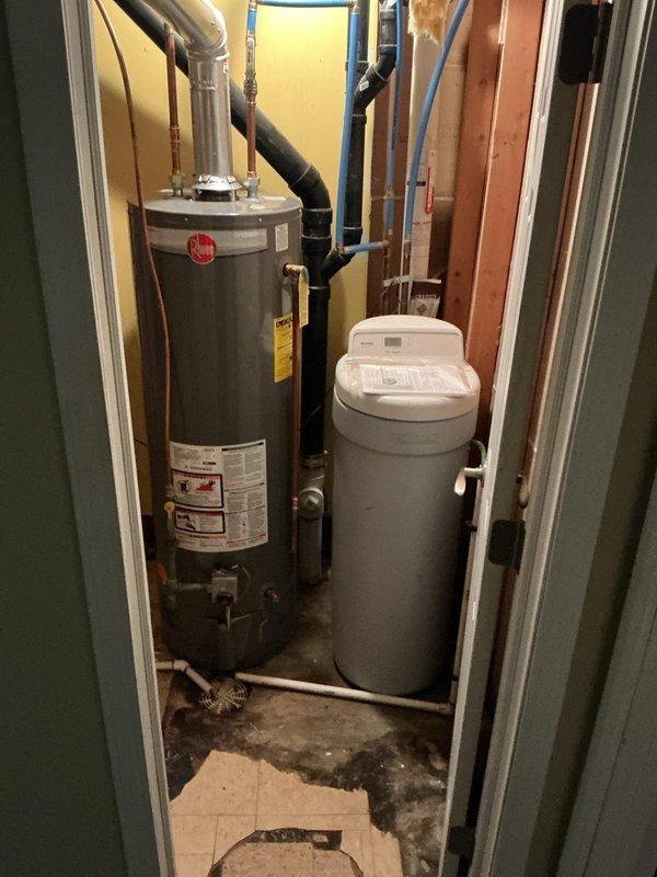 Responded to a water softener leak at a vacant property where the unit and main water line had been shut off as a precautionary measure. Conducted diagnostic inspection of the water treatment system and identified active leaking from the intake connection on the water softener head assembly. Upon further examination, discovered significant mold growth surrounding the softener head unit, indicating prolonged moisture exposure. Due to the extent of water damage and biological contamination present, recommended complete water softener replacement rather than repair. No repair work was performed on-site; documented findings with photographs showing the affected equipment, visible floor staining from water damage, and overall system condition. Case forwarded for water softener replacement quote and installation scheduling.