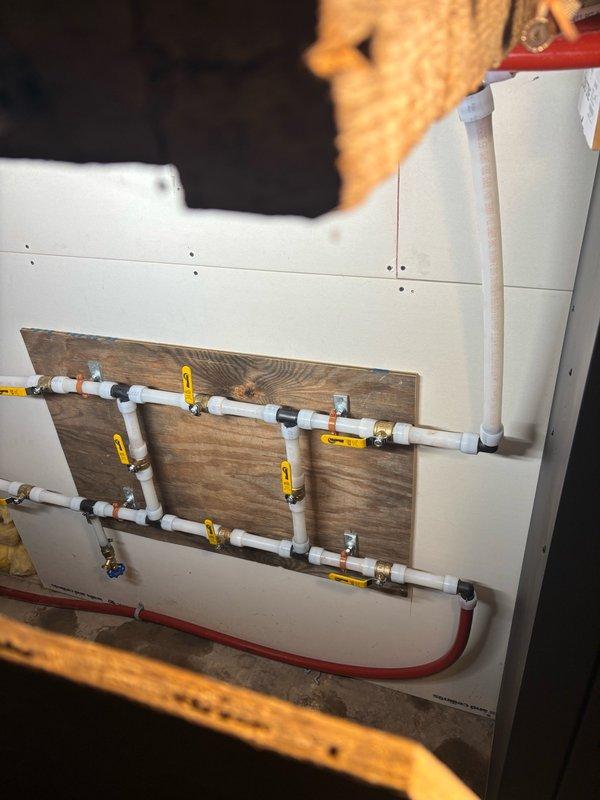 # Boiler System Re-Piping

Completed comprehensive re-piping of both indoor and outdoor boiler systems. Installed new PVC manifold distribution system with multiple zone controls, featuring yellow-handled ball valves at each branch for individual flow management. Mounted entire assembly on wooden backing board with proper support and secured all connections with appropriate PVC and brass fittings for long-term reliability.