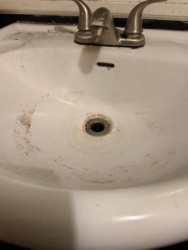 Responded to service call for shower leak and clogged sink. Upon inspection, identified leaking shower valve at cartridge port and backed-up downstairs vanity drain with leaking drain assembly. Attempted extraction of old Moen cartridge, but cartridge was seized and would not move. Determined full shower valve replacement necessary. Provided estimates for shower valve replacement and vanity drain repair. Photographed existing conditions showing stained vanity sink with dual-handle faucet and compromised drain assembly, as well as tub/shower access point with exposed valve assembly behind wall. Ordered required parts for valve replacement and scheduled return visit to complete installation upon parts arrival.