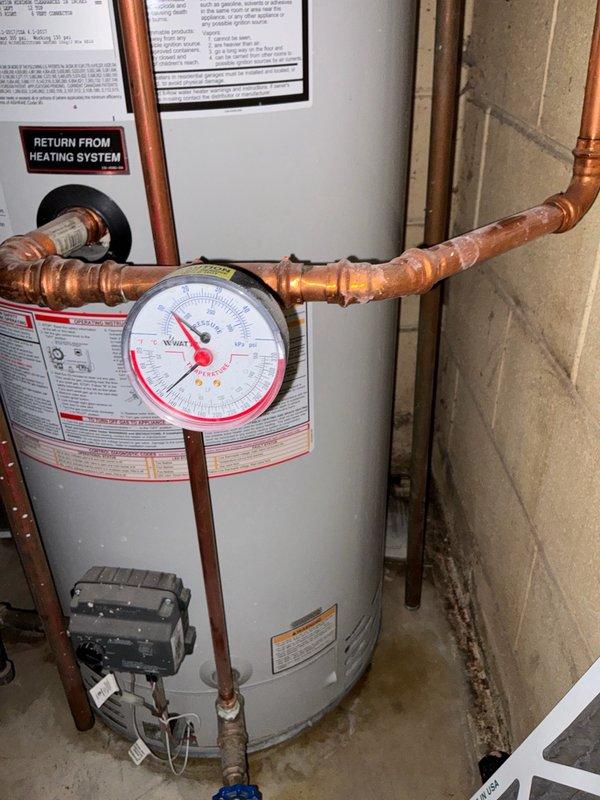Responded to service call for water heater leaking from bottom. Upon arrival, performed comprehensive diagnostic assessment of residential tanked water heater system installed in basement utility area. Inspected entire unit including tank integrity, copper piping connections, pressure relief valve, gas valve assembly, and all associated fittings. Examined pressure gauge readings and verified proper system operation of heating components. Documented existing installation configuration including return lines from heating system, soldered copper joints, and control unit functionality. Evaluated water heater for signs of corrosion, structural compromise, and potential leak sources at base of tank. Photographed installation for diagnostic documentation showing pressure monitoring equipment, piping layout, and overall system condition. Provided detailed estimate for recommended repairs or replacement options based on assessment findings.