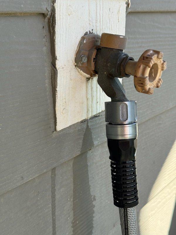 Responded to service call for outdoor faucet experiencing seasonal leaking and two indoor faucets with suspected cartridge failures. Replaced outdoor spigot assembly mounted on exterior wall, including installation of new brass valve body with cross-handle and connection to existing flexible braided supply line via adapter fittings. Addressed water intrusion issues affecting the mounting area on white wooden trim. Inspected and serviced interior plumbing connections in utility access area, working with PVC supply lines and flexible braided hoses connected to wooden platform assembly. All connections tested for proper operation and leak-free performance upon completion.