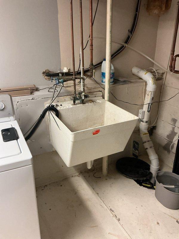 Completed installation of new single basin laundry tub system in utility room. Installed white fiberglass utility sink with mounting legs, top-mount faucet assembly, washing machine supply valves with shut-off stops, and complete drain assembly with PVC drainage piping. All plumbing connections secured to existing copper supply lines and drainage system, tested for proper operation and verified no leaks.