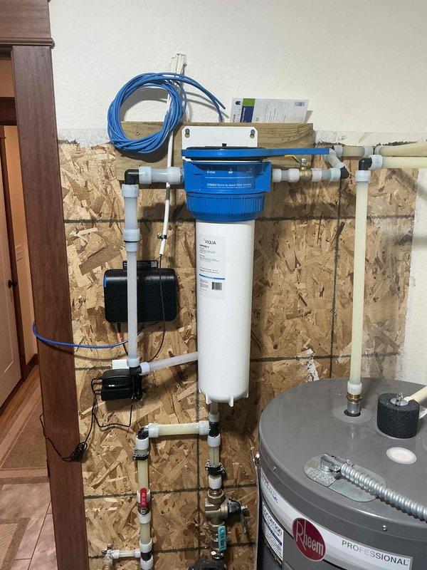 Completed installation of whole-house 20-inch water filtration system with blue cap housing and white cylindrical filter cartridge, integrated into existing plumbing configuration with white PVC piping and multiple shutoff valves. Performed plumbing inspection and installed expansion tank in conjunction with Rheem Professional water heater system, ensuring proper pressure regulation and water quality treatment throughout the residence.