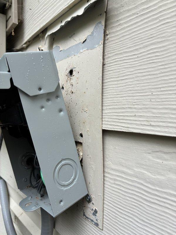 Responded to callback regarding improperly mounted electrical disconnect box on exterior siding. Upon arrival, addressed customer concerns about disconnect installation and discovered significant water damage and deteriorated siding material behind the unit. After consulting with customer, removed disconnect box from wall mounting to allow access for proper flashing installation and siding repair. Disconnect left temporarily suspended by electrical whip to maintain power while customer completes necessary flashing work behind box location. Customer will reinstall disconnect upon completion of weatherproofing repairs. Documented existing conditions including exposed underlayment damage, deteriorated wall board, and compromised siding integrity around mounting area.