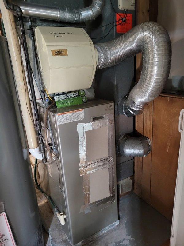 Performed furnace maintenance inspection on a 23-year-old Bryant heating system. Upon examination, discovered a failed heat exchanger with visible nodules present, indicating a critical safety concern requiring immediate attention. Inspection was halted at homeowner's request as they decided to proceed with full system replacement. Documented equipment condition with photographs showing the furnace unit with Aprilaire whole-house humidifier and associated ductwork in basement utility area. Additional photos captured attic ductwork assembly showing age-related deterioration and dust accumulation. Noted mildew odor present when air conditioning operates, likely related to condensate drainage issues. Observed humidifier leaking and drain tube requiring thorough cleaning. Furnace filter was found to be excessively dusty. Recommended comfort advisor consultation for system replacement options due to failed heat exchanger rendering current unit unsafe for operation.