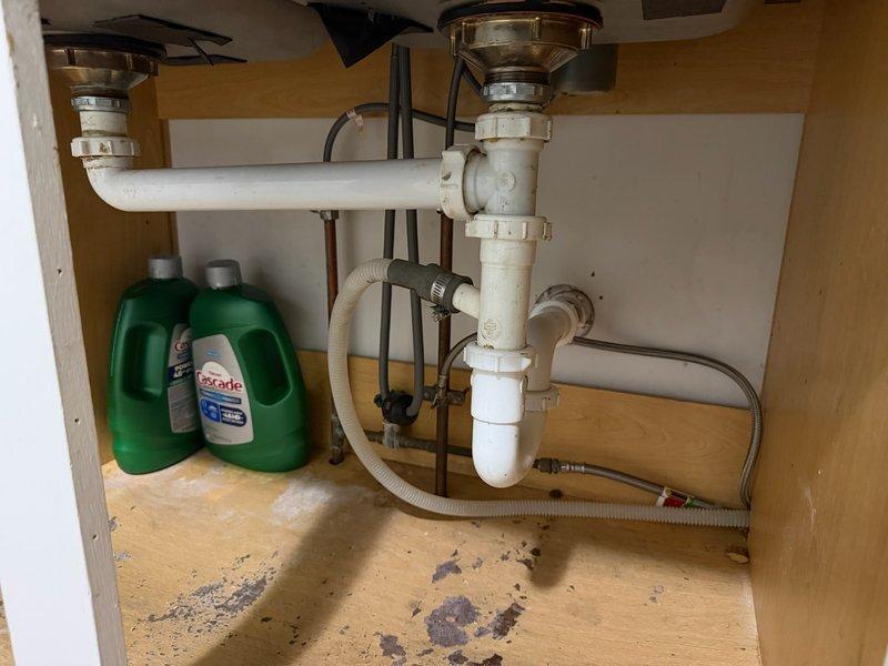Responded to service call for intermittent water leak under kitchen sink. Upon inspection, found faulty continuous waste drain connections between double sink basins that were separating and causing leakage. Replaced existing PVC drain piping assembly including P-trap configuration and connection points. Secured all pipe connections with proper clamps to prevent future separation. Tested system for proper drainage and verified no leaks present at all connection points.