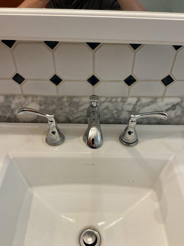 Responded to service call for dripping bathroom faucet with compromised plumbing components resulting from attempted self-repair. Main water supply had been shut off due to failed repair attempt. Removed existing faulty shut-off valves and supply lines. Installed new Keeney shut-off valves and supply lines to restore proper water control and flow. Completed part order form for replacement three-piece chrome faucet assembly to be installed on white Kohler rectangular basin sink with octagonal tile backsplash. System tested and ready for final faucet installation upon part arrival.