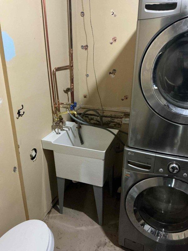 Installed a new freestanding Mustee laundry sink with faucet deck mount in utility room. Connected new hook-up lines for washer machine water supplies, including copper piping with shutoff valves. Installation completed per specifications with all plumbing connections secured and tested for proper operation.