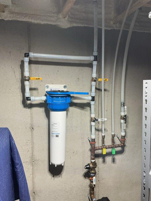 Installed a whole home carbon water filtration system with blue cap housing, mounting brackets, and white PVC supply piping to main water line. Added thermal expansion tank to water heating system to comply with Wisconsin Administrative Code SPA 382.40(3)(c)4, as existing pressure reducer on main line created a closed-loop system without proper expansion protection. Connected expansion tank with appropriate PVC piping and brass fittings, securing unit to wall framing adjacent to water heater. All installations completed per approved estimate with proper mounting, connections, and shutoff valves for future maintenance access.