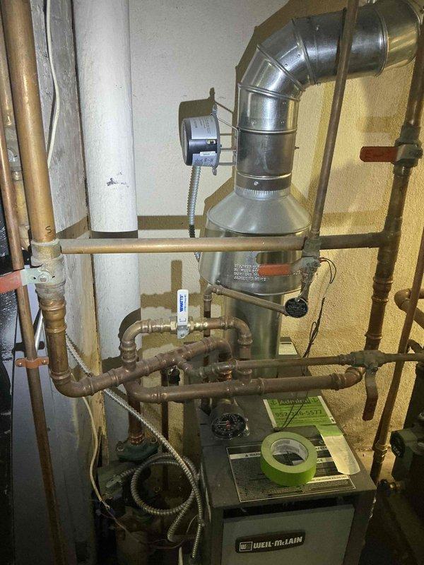 Responded to service call for Weil-McLain boiler system with active water leaks. Upon inspection, found disconnected radiator supply line at floor level and failed radiator valve causing system to leak when operated. Documented existing conditions including aged copper piping with significant corrosion and deterioration throughout distribution system. Assessed boiler unit, circulation components, and venting system. Photographed installation for estimate preparation. Recommended complete repair of broken radiator line, replacement of defective radiator valve, and evaluation of additional piping concerns due to advanced age and condition of system components.