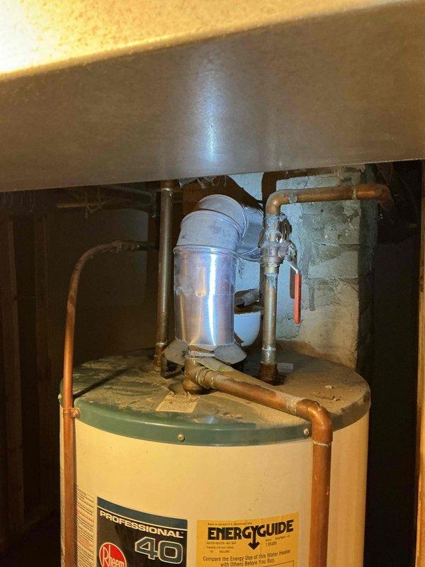 Responded to service call for water heater venting issue in residential basement. Upon inspection, identified improper back-venting condition on natural gas standard atmospheric vent water heater causing drafting problems. Corrected venting configuration to ensure proper draft and safe exhaust of combustion gases. Verified unit operation and proper venting performance upon completion. Documented existing 40-gallon tank water heater installation with standard copper supply line connections and expansion tank present. All work performed in accordance with current plumbing and mechanical codes for natural gas appliance venting requirements.